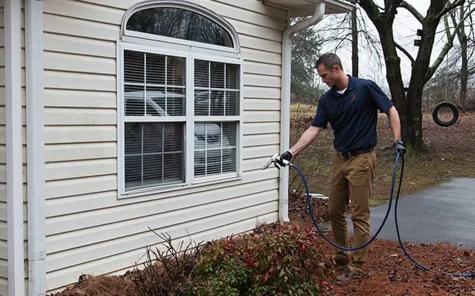 A technician spraying a liquid flea treatment around the exterior foundation and garden beds of a home.